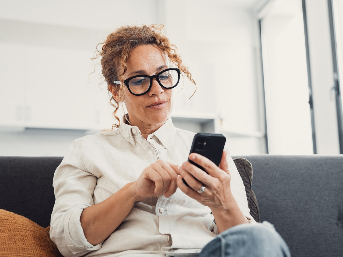 A woman sitting on a sofa, looking at her phone with a thoughtful expression.