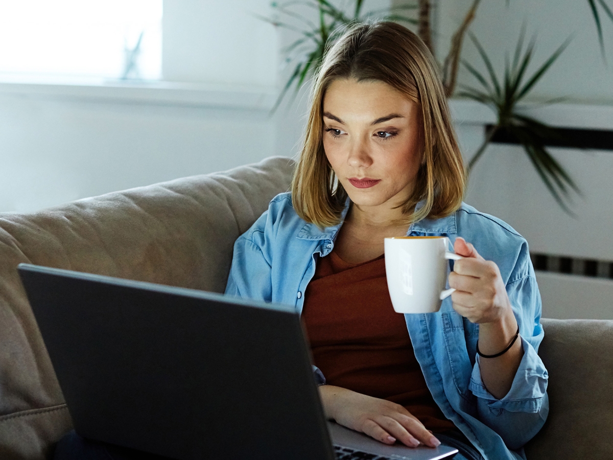 Focused woman holding a cup and looking at her laptop screen